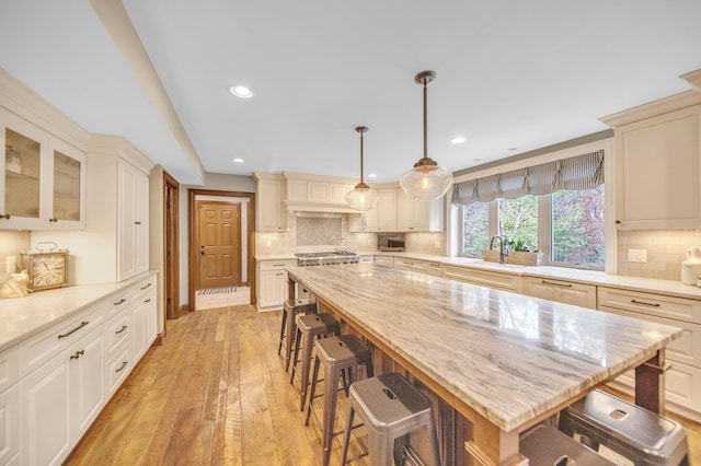 kitchen featuring recessed lighting, decorative backsplash, a breakfast bar area, light wood finished floors, and a sink