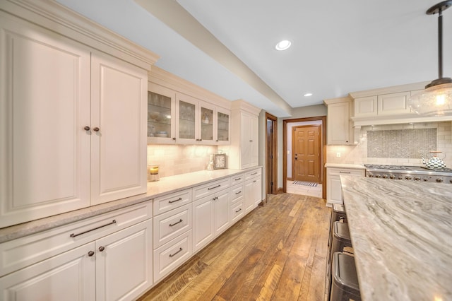 kitchen featuring recessed lighting, light wood finished floors, glass insert cabinets, and backsplash
