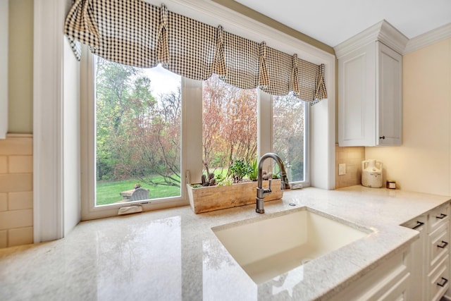 room details featuring backsplash, a sink, light stone counters, and white cabinetry