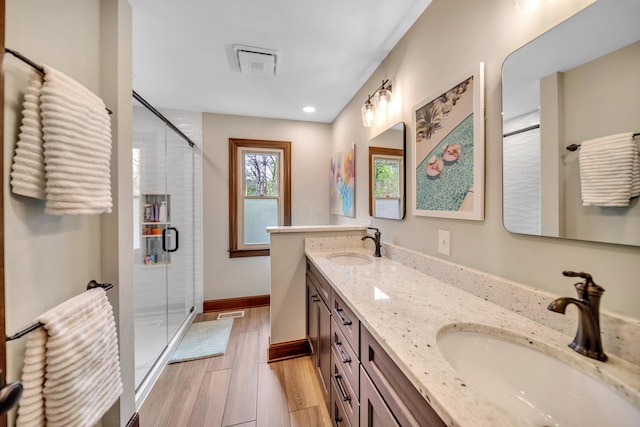full bath featuring a stall shower, wood finished floors, double vanity, and a sink