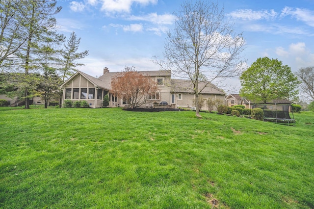 back of property with a chimney, a yard, a sunroom, and a trampoline