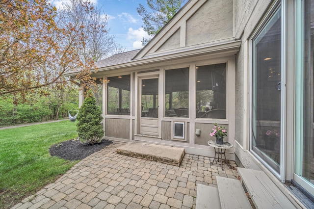 view of exterior entry with a yard, a shingled roof, and a patio area