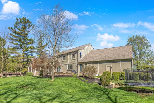 rear view of house featuring a lawn, stucco siding, and a trampoline