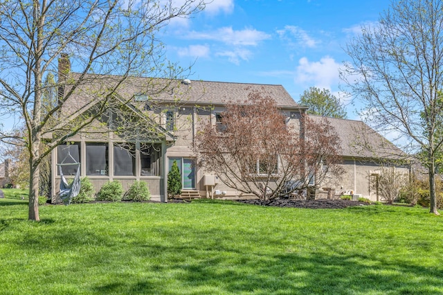 rear view of house with a chimney, entry steps, a sunroom, and a lawn