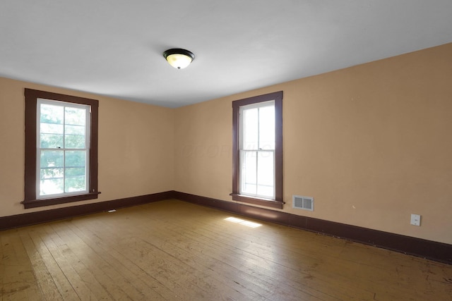 empty room featuring baseboards, visible vents, a wealth of natural light, and hardwood / wood-style flooring