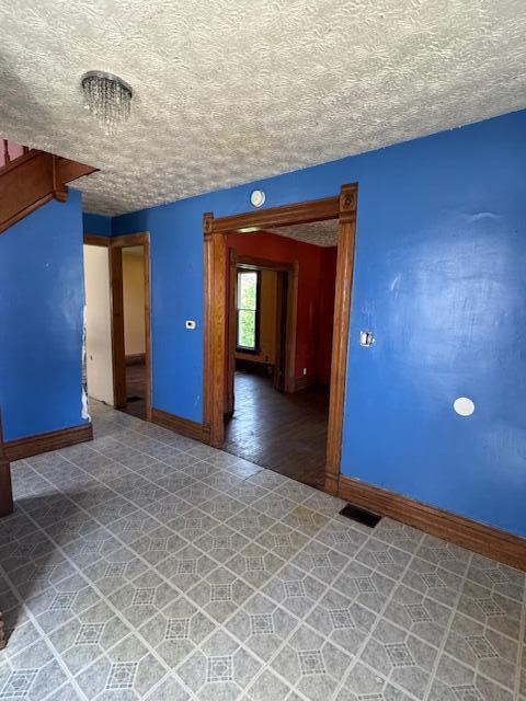 unfurnished room featuring a textured ceiling, visible vents, and baseboards