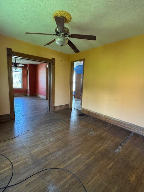 unfurnished room featuring dark wood-type flooring, ceiling fan, a textured ceiling, and baseboards