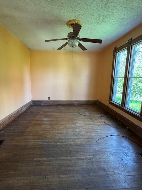unfurnished room featuring a textured ceiling, ceiling fan, dark wood-style floors, and baseboards