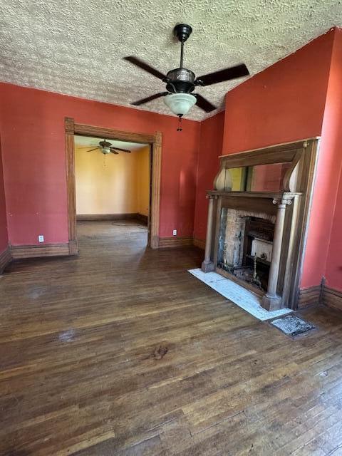 unfurnished living room with dark wood-style floors, ceiling fan, a fireplace with flush hearth, and baseboards