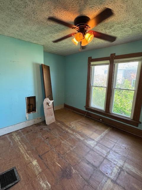 unfurnished room with a ceiling fan, visible vents, a textured ceiling, and baseboards