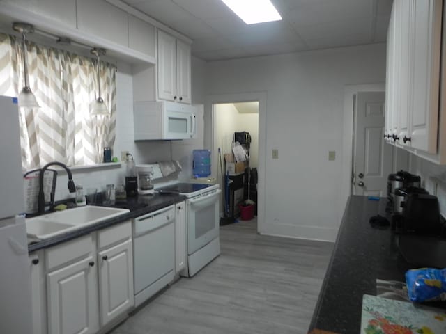kitchen with dark countertops, light wood-type flooring, a sink, white appliances, and white cabinetry