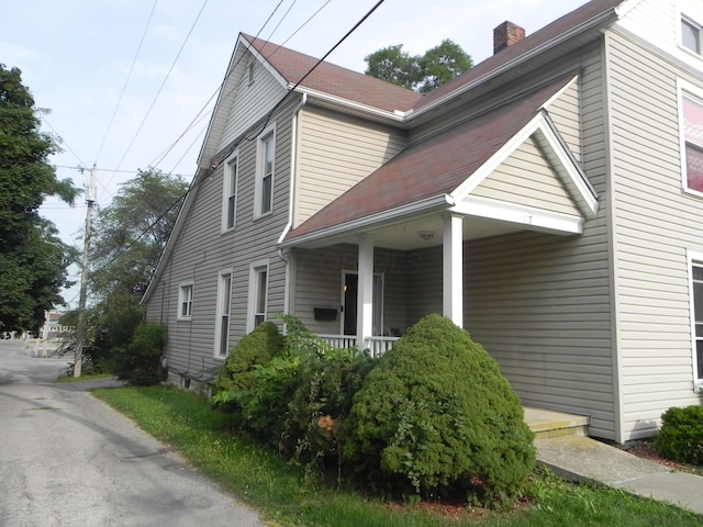 view of side of home featuring covered porch and a chimney