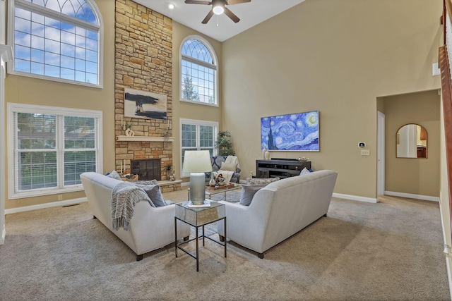 living area featuring a ceiling fan, a stone fireplace, a towering ceiling, baseboards, and carpet floors