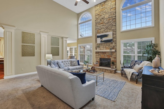 living room with a high ceiling, ceiling fan, carpet floors, a stone fireplace, and baseboards