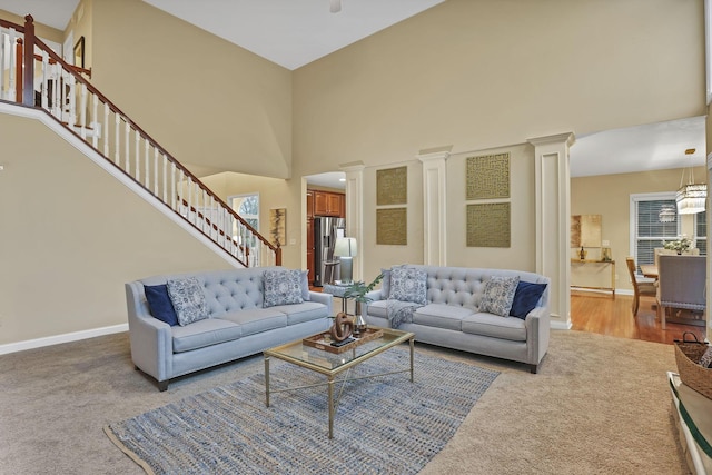 carpeted living area featuring stairs, ornate columns, baseboards, and a towering ceiling