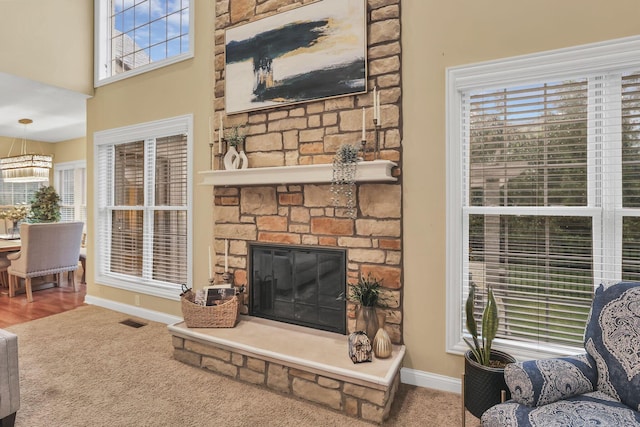 carpeted living area with baseboards, plenty of natural light, a stone fireplace, and visible vents