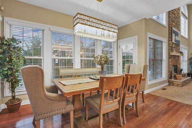 dining space featuring wood-type flooring, baseboards, a fireplace, and an inviting chandelier