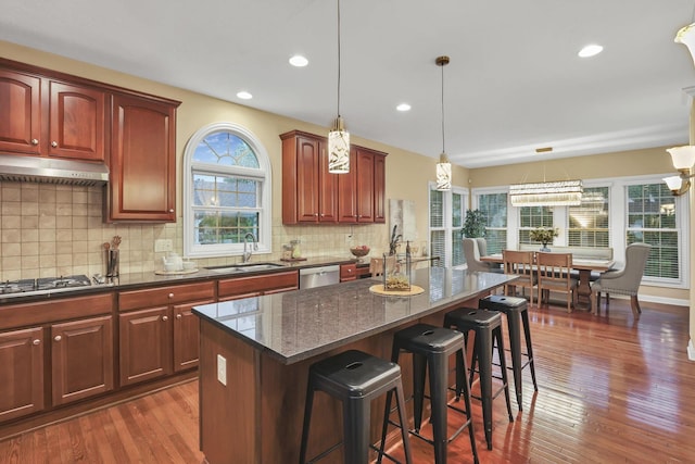kitchen with a kitchen island, a breakfast bar, under cabinet range hood, a sink, and appliances with stainless steel finishes