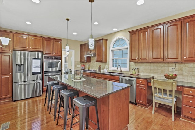 kitchen featuring a sink, light wood finished floors, stainless steel appliances, a kitchen bar, and visible vents