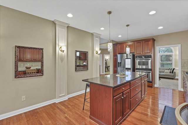 kitchen featuring light wood-type flooring, baseboards, appliances with stainless steel finishes, and a kitchen breakfast bar