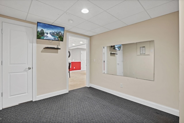 empty room featuring baseboards, a drop ceiling, and dark colored carpet