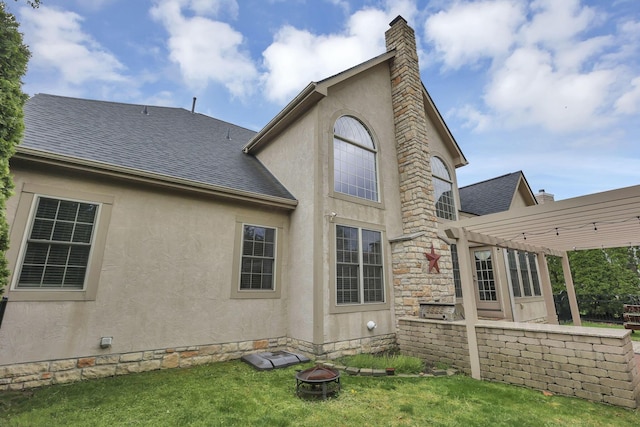 back of property with a fire pit, a pergola, roof with shingles, stucco siding, and a chimney