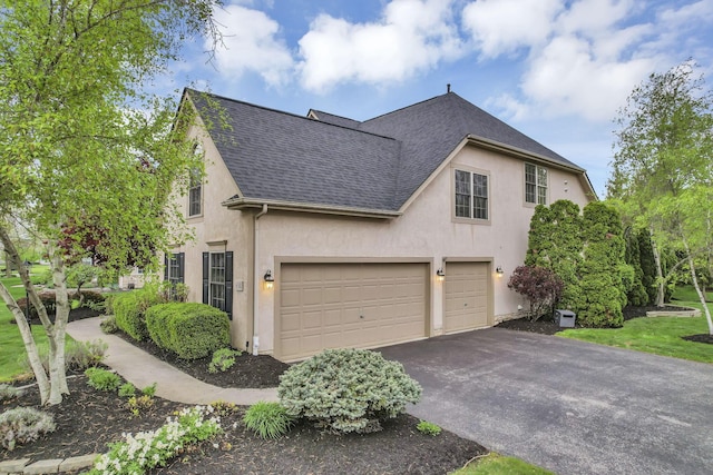 view of side of home with an attached garage, a shingled roof, aphalt driveway, and stucco siding