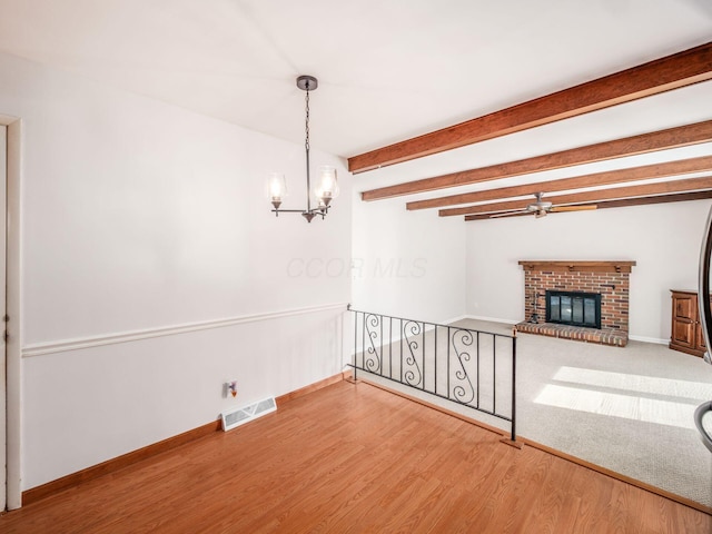 spare room with visible vents, a brick fireplace, wood finished floors, beamed ceiling, and an inviting chandelier