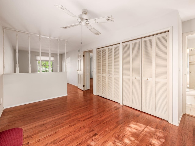 unfurnished bedroom with ceiling fan, two closets, baseboards, wood finished floors, and ensuite bathroom