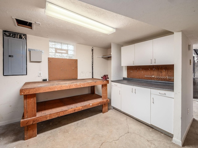 below grade area featuring baseboards, electric panel, a textured ceiling, and a workshop area