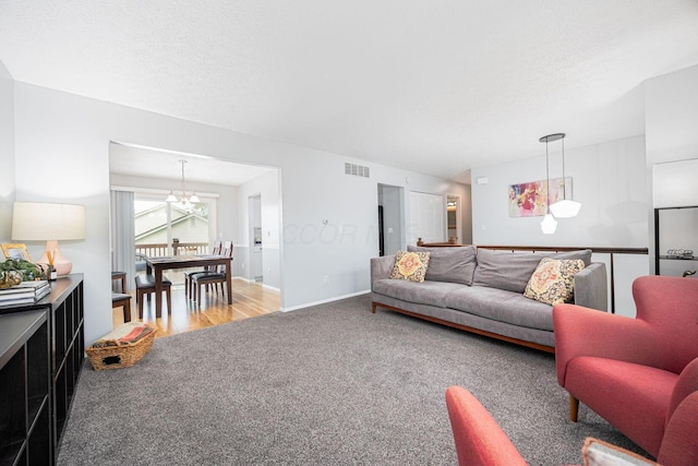 carpeted living area with a textured ceiling, visible vents, wood finished floors, baseboards, and a notable chandelier