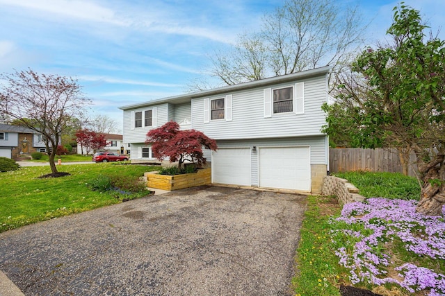 split foyer home featuring fence, an attached garage, driveway, and a front lawn