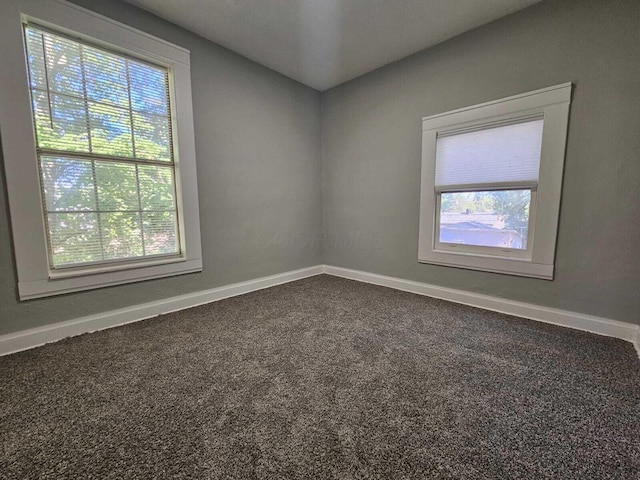 unfurnished room featuring baseboards, a wealth of natural light, and dark colored carpet