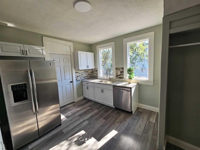 kitchen featuring decorative backsplash, dark wood-type flooring, white cabinetry, a sink, and stainless steel appliances