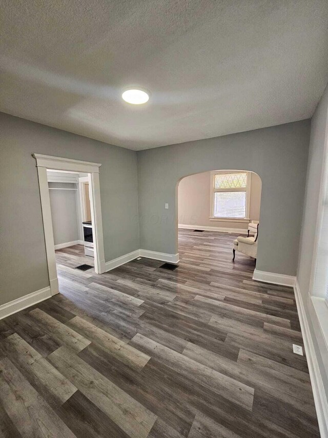 empty room with arched walkways, baseboards, a textured ceiling, and wood finished floors