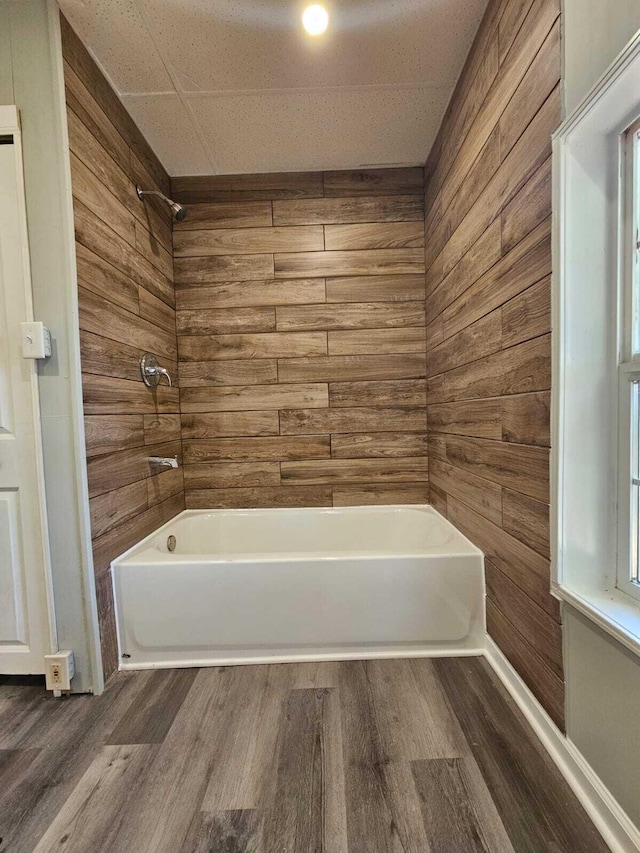 bathroom featuring shower / bathtub combination, wood walls, and wood finished floors