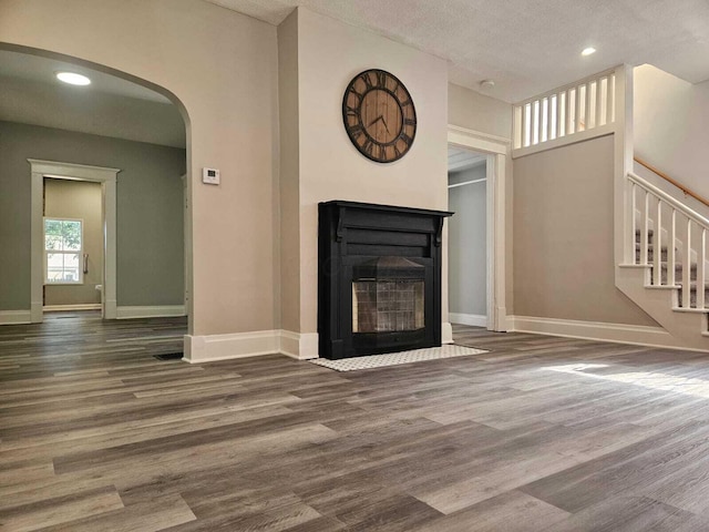 unfurnished living room with baseboards, arched walkways, stairs, and wood finished floors