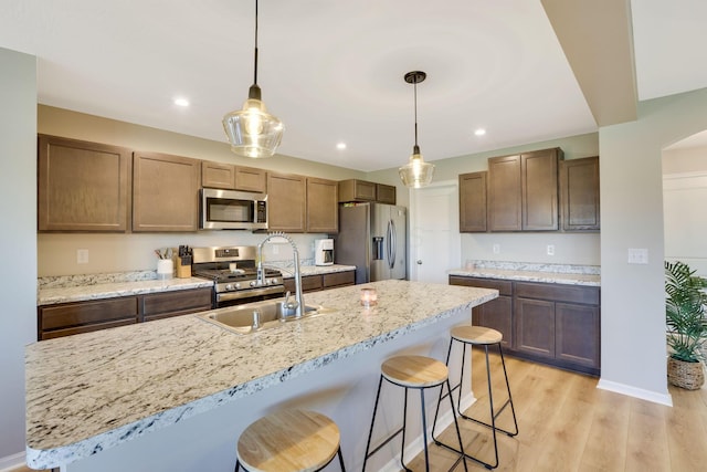 kitchen featuring hanging light fixtures, a sink, light wood finished floors, a breakfast bar area, and stainless steel appliances
