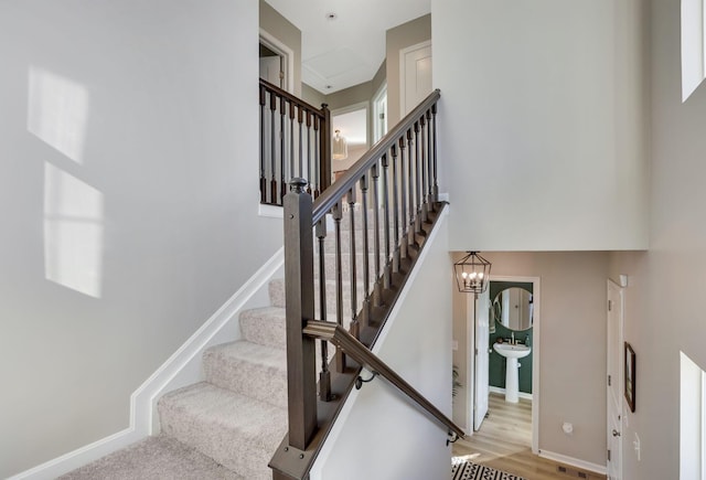 stairway with baseboards, a chandelier, wood finished floors, and a towering ceiling