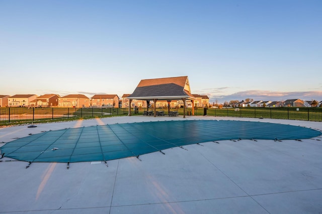 pool at dusk featuring fence, a residential view, a gazebo, a fenced in pool, and a patio
