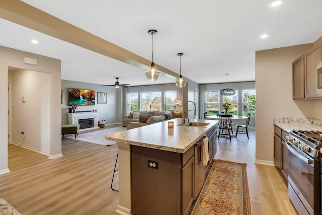 kitchen featuring a glass covered fireplace, a kitchen island with sink, light wood-style floors, stainless steel range with gas stovetop, and a sink