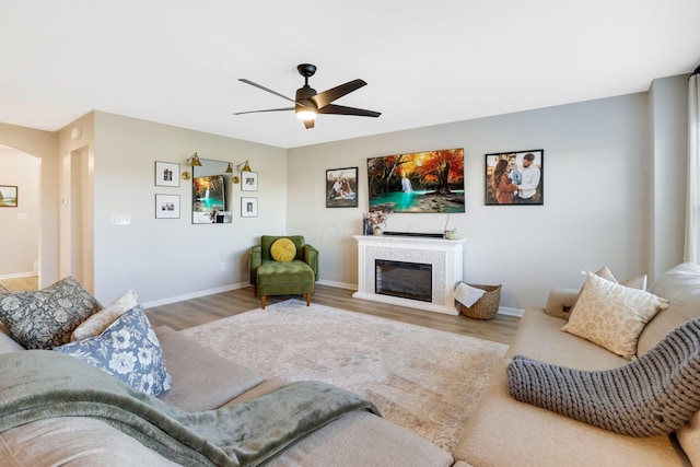 living room with arched walkways, a glass covered fireplace, a ceiling fan, baseboards, and wood finished floors