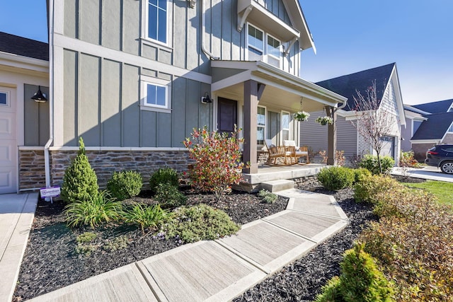 entrance to property featuring board and batten siding, covered porch, stone siding, and a garage