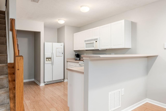 kitchen featuring visible vents, a peninsula, light wood finished floors, white appliances, and white cabinetry
