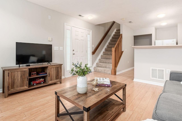 living area featuring stairs, baseboards, visible vents, and light wood-style flooring