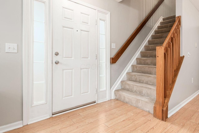 foyer with light wood-type flooring, stairs, and baseboards