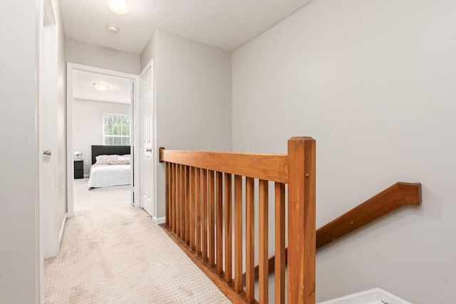 hallway featuring baseboards, carpet flooring, and an upstairs landing
