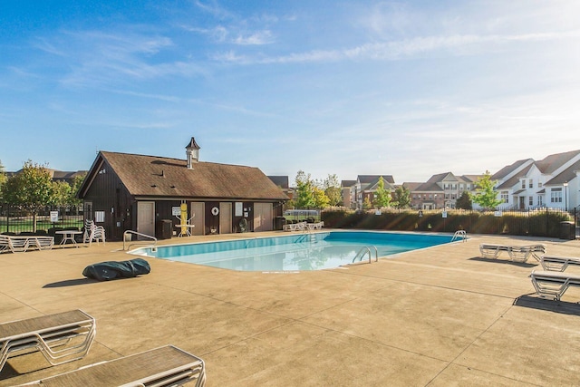 community pool with a patio, fence, and a residential view