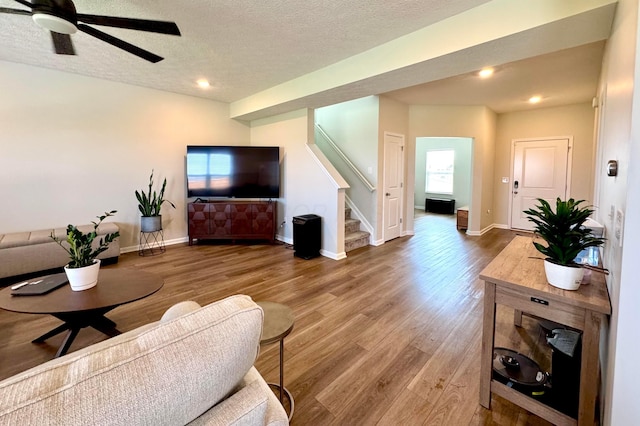 living area featuring stairs, a ceiling fan, baseboards, and wood finished floors