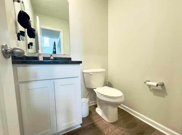 half bath featuring toilet, baseboards, wood finished floors, and vanity